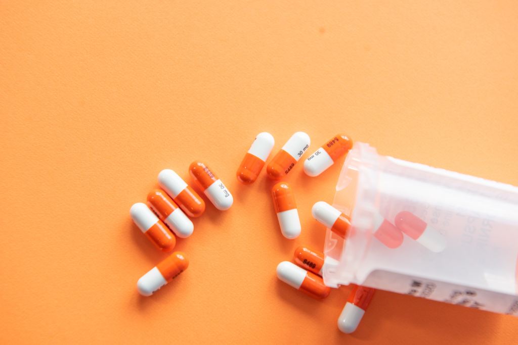 A pill bottle with pills spilling out on an orange background.
Image sourced via Unsplash.